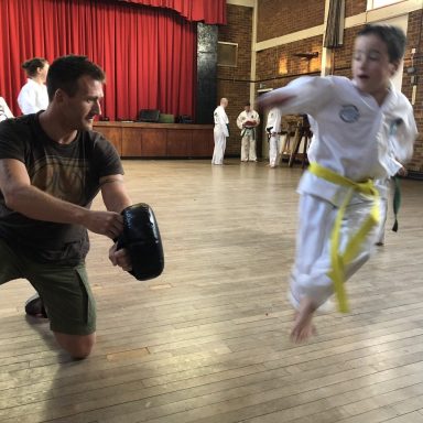 Surrey Taekwon-Do boy student performing a kick with instructor holding a kicking pad