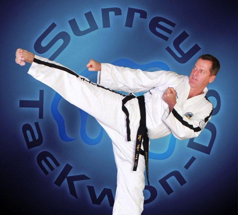 VII Dan Surrey Taekwon-Do instructor Richard Hamilton executing a kicking move with Surrey Taekwon-Do logo in background