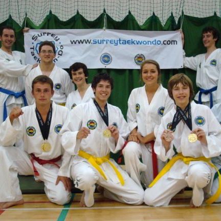 Surrey Taekwon-Do medal winners holding their medals, smiling at camera with banner behind